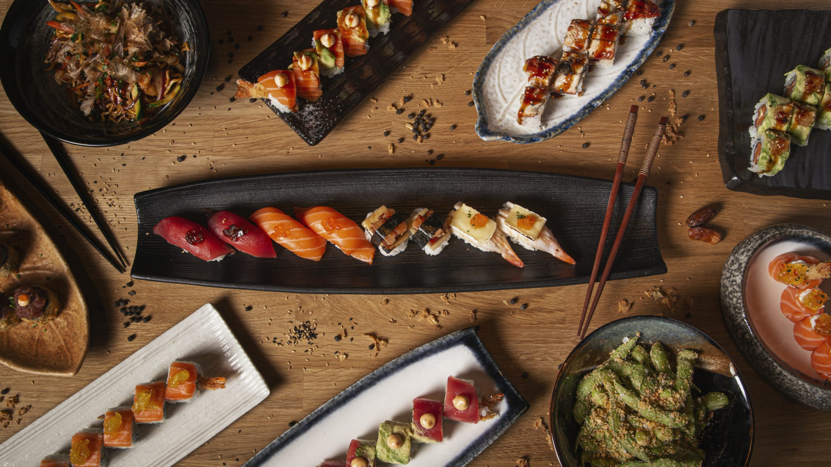 A top view of a variety of sushi, nigiri, sashimi, yakisoba and edamame on a restaurant wooden table